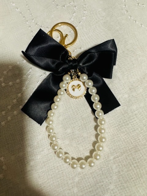 Luxury designer keychain featuring a black satin bow, gold keyring, and pearl bead wristlet strap with gold bow charm
