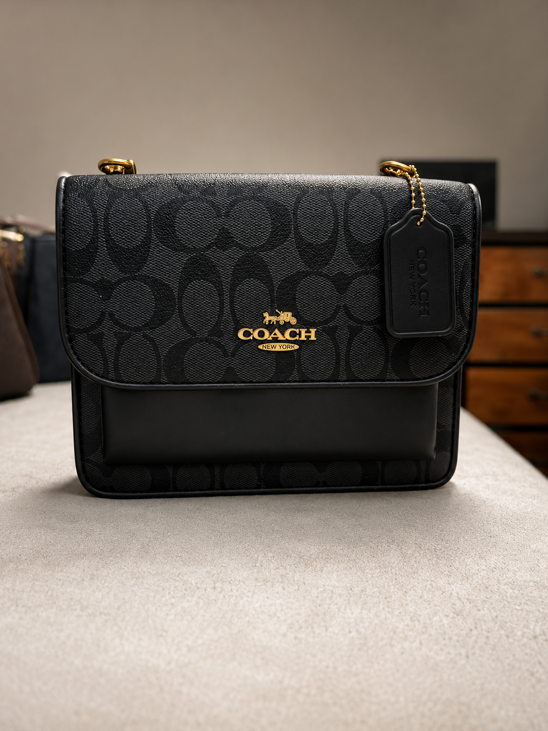 Coach black signature monogram crossbody bag with gold hardware embossed leather front pocket chain strap leather tag with COACH branding on neutral surface