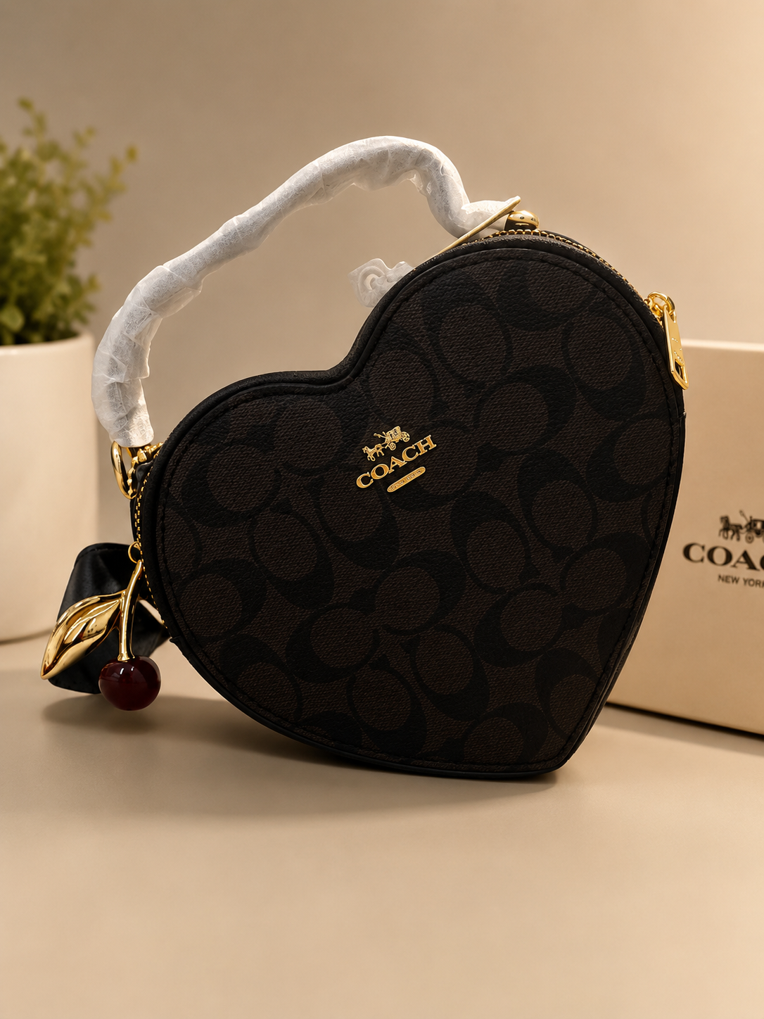 Coach black signature monogram heart-shaped bag with gold cherry charm keychain white wrapped top handle zipper closure and COACH box in background