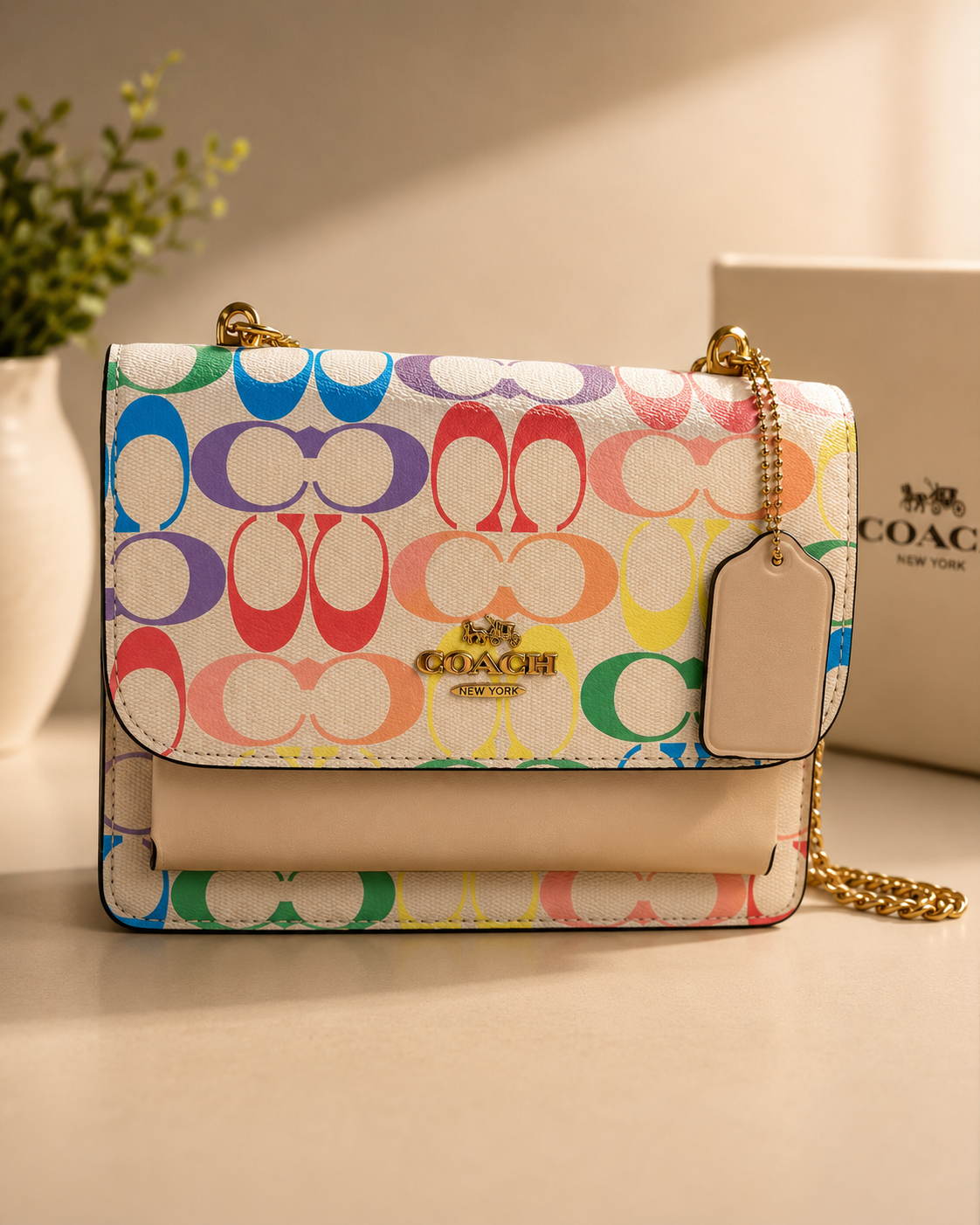 Coach rainbow multicolor signature shoulder bag featuring vibrant red blue green yellow purple logo pattern on cream base with gold chain strap leather tag and COACH box in background