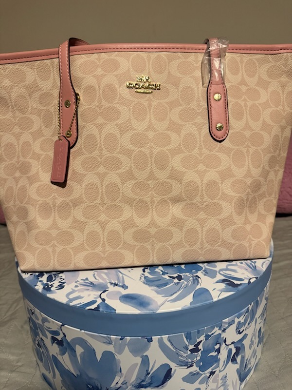 Beige tan Coach signature monogram tote bag with pink rose leather handle accents gold COACH logo hardware dual top handles displayed on blue floral box