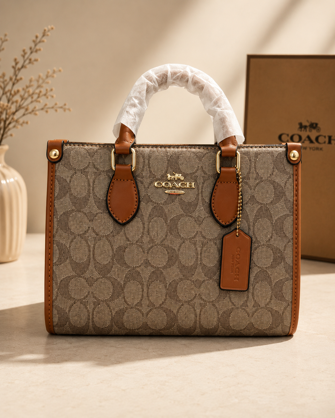 Coach beige tan signature monogram structured tote bag with brown leather trim dual top handles gold buckle hardware protective handle wrapping and leather tag on neutral surface