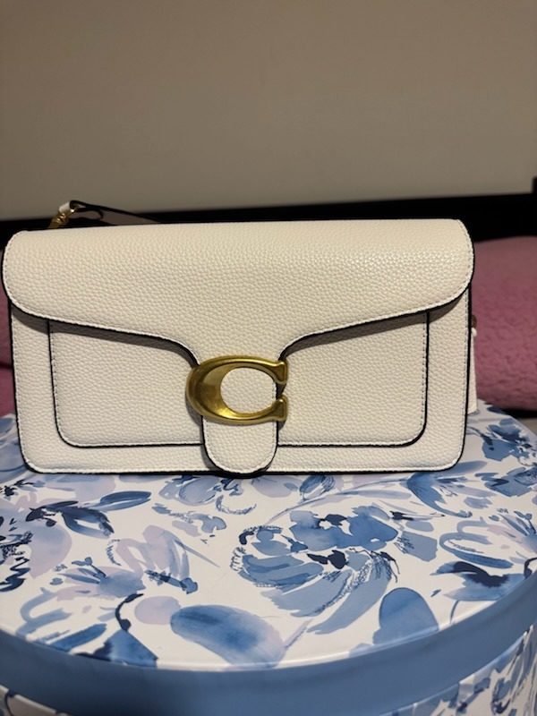 White cream Coach leather textured shoulder bag with large gold C buckle hardware flap closure structured design displayed on blue white floral patterned box