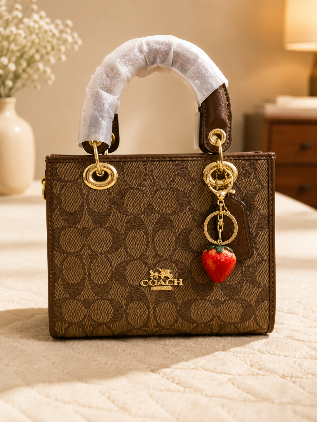 Brown Coach monogram tote bag with gold hardware and strawberry charm keychain, designer handbag with top handle