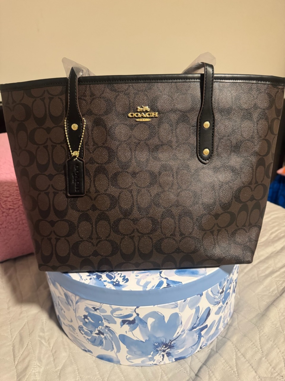 Dark brown black Coach signature monogram tote bag with dark leather handle accents gold COACH logo hardware dual top handles leather tag with chain on blue floral display box