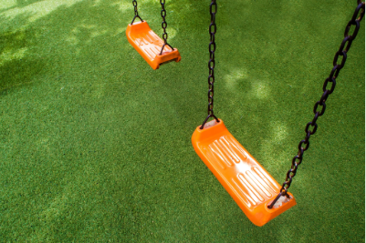 Orange swing seats hanging over artificial turf surrounding a playground area