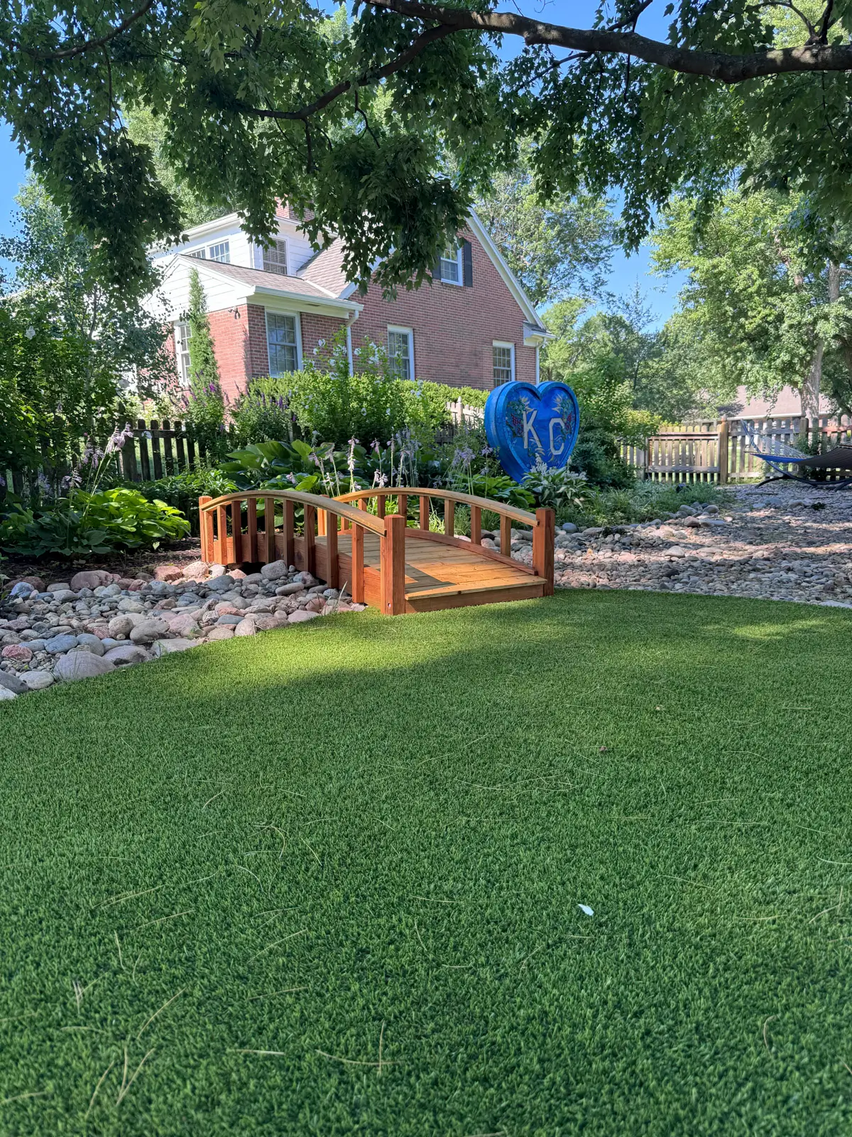 Artificial turf installed in shaded area beneath trees with bridge and KC heart sculpture