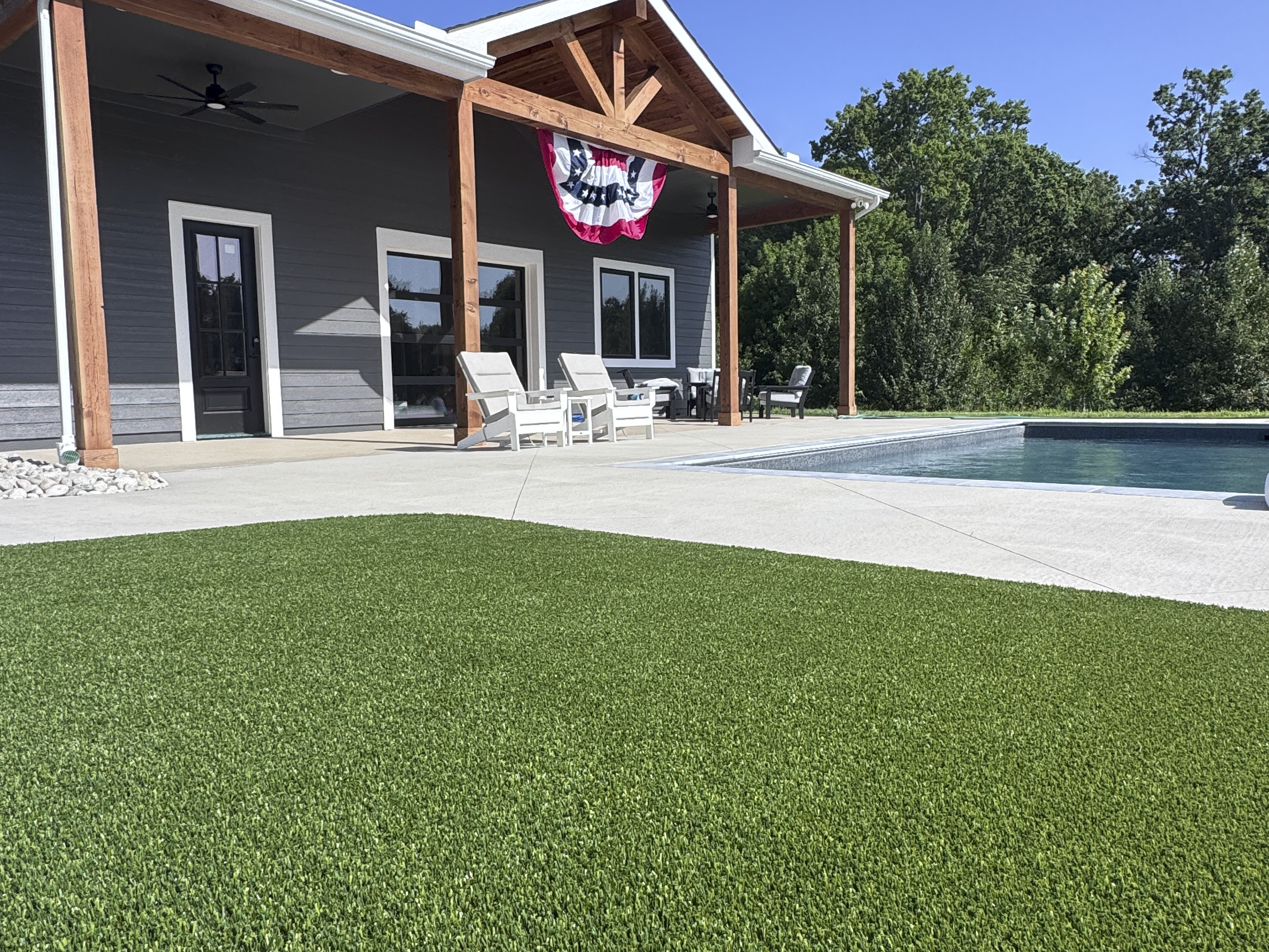 Artificial turf installed between large pavers beside a pool with patio seating