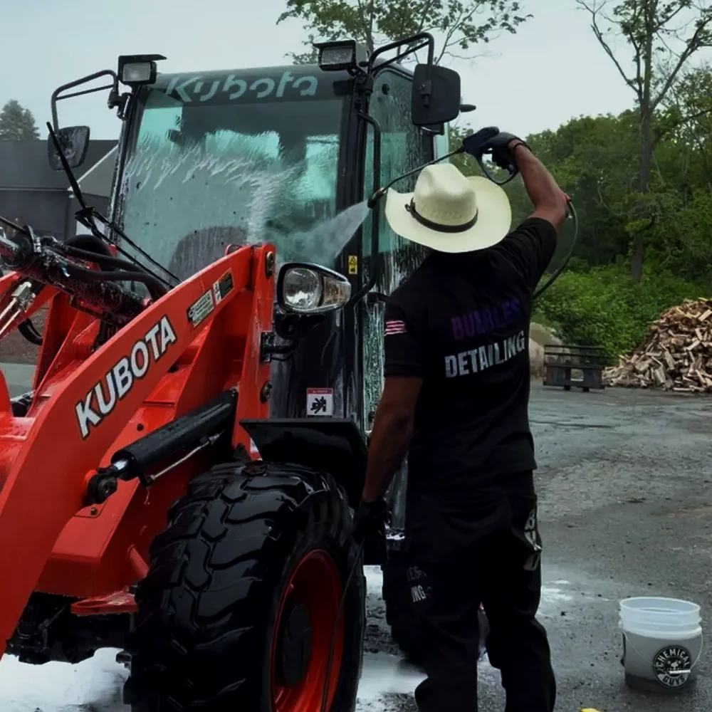 Isaiah pressure washing a red Kubota loader during mobile fleet detailing service in West Bridgewater MA