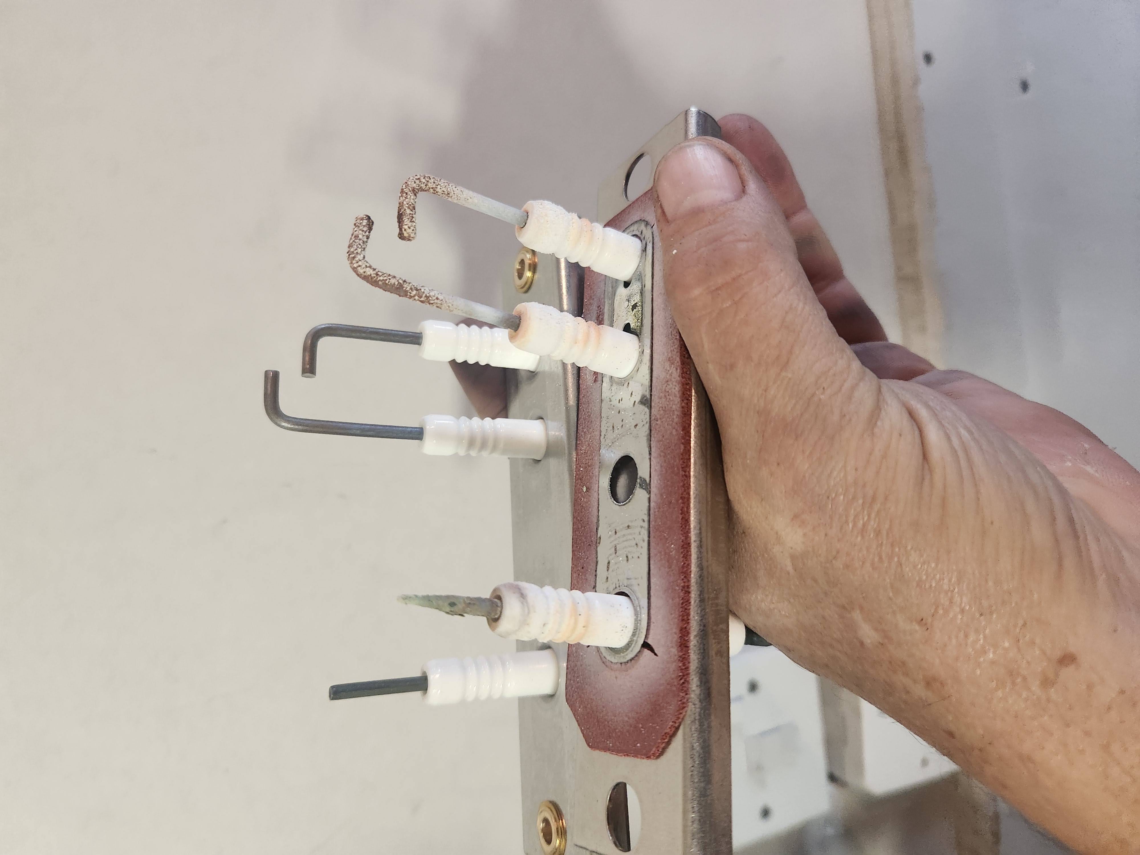 Hand holding a gas ignition electrode assembly showing worn ceramic insulators during boiler servicing.