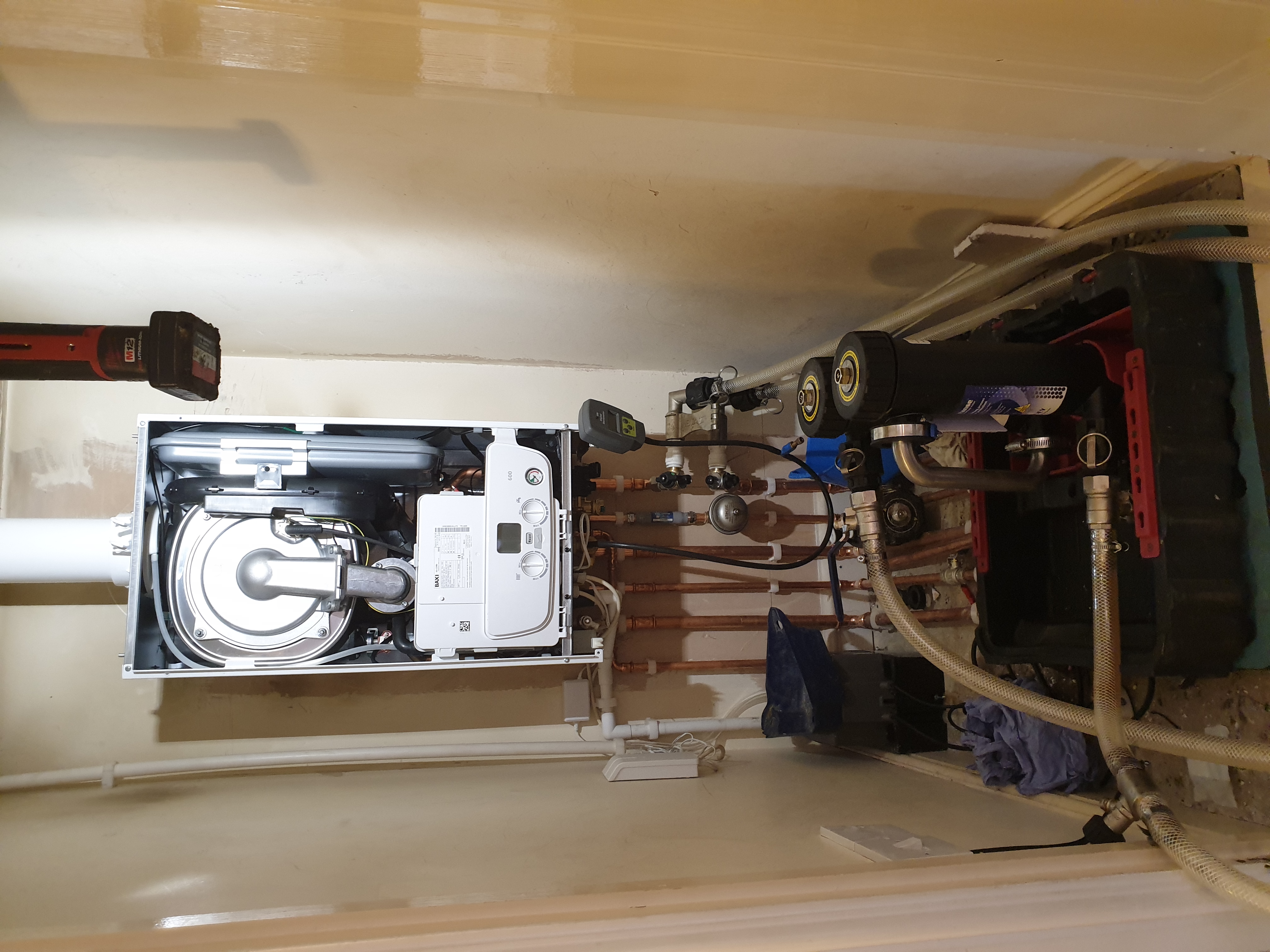 Baxi combi boiler installed in a utility cupboard alongside a large unvented hot water cylinder with extensive copper pipework and system controls.