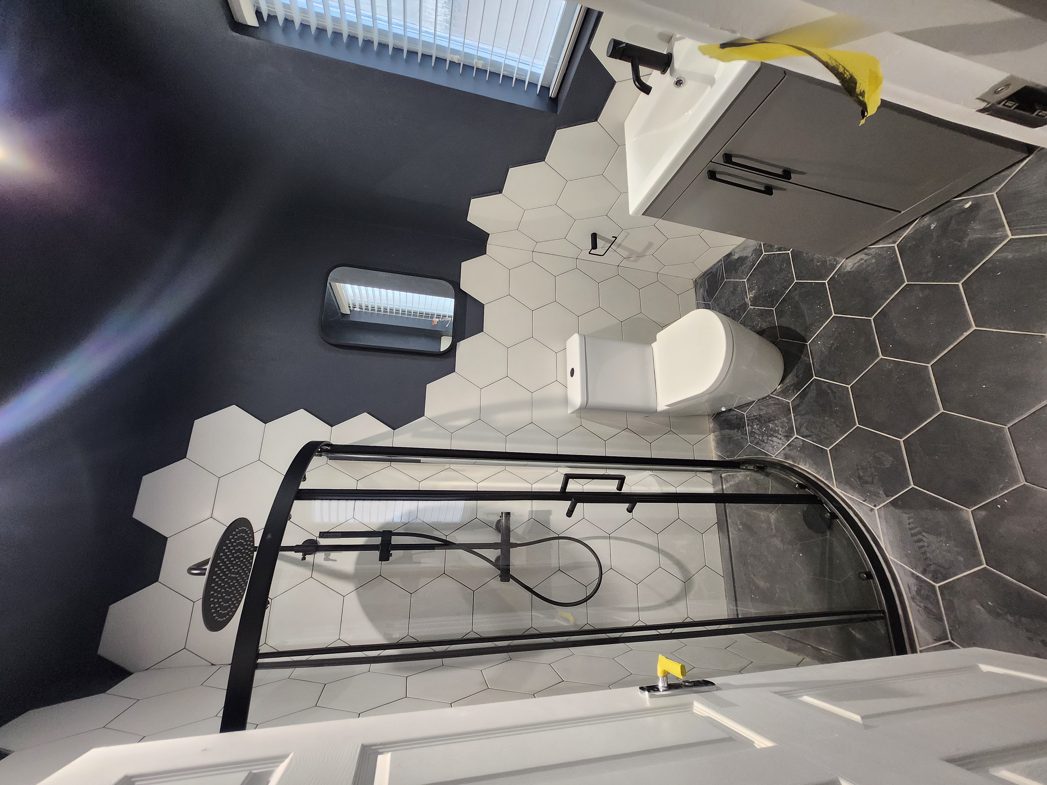 Contemporary bathroom featuring white hexagonal wall tiles, wall-hung toilet, curved glass shower enclosure and matte-black fittings.