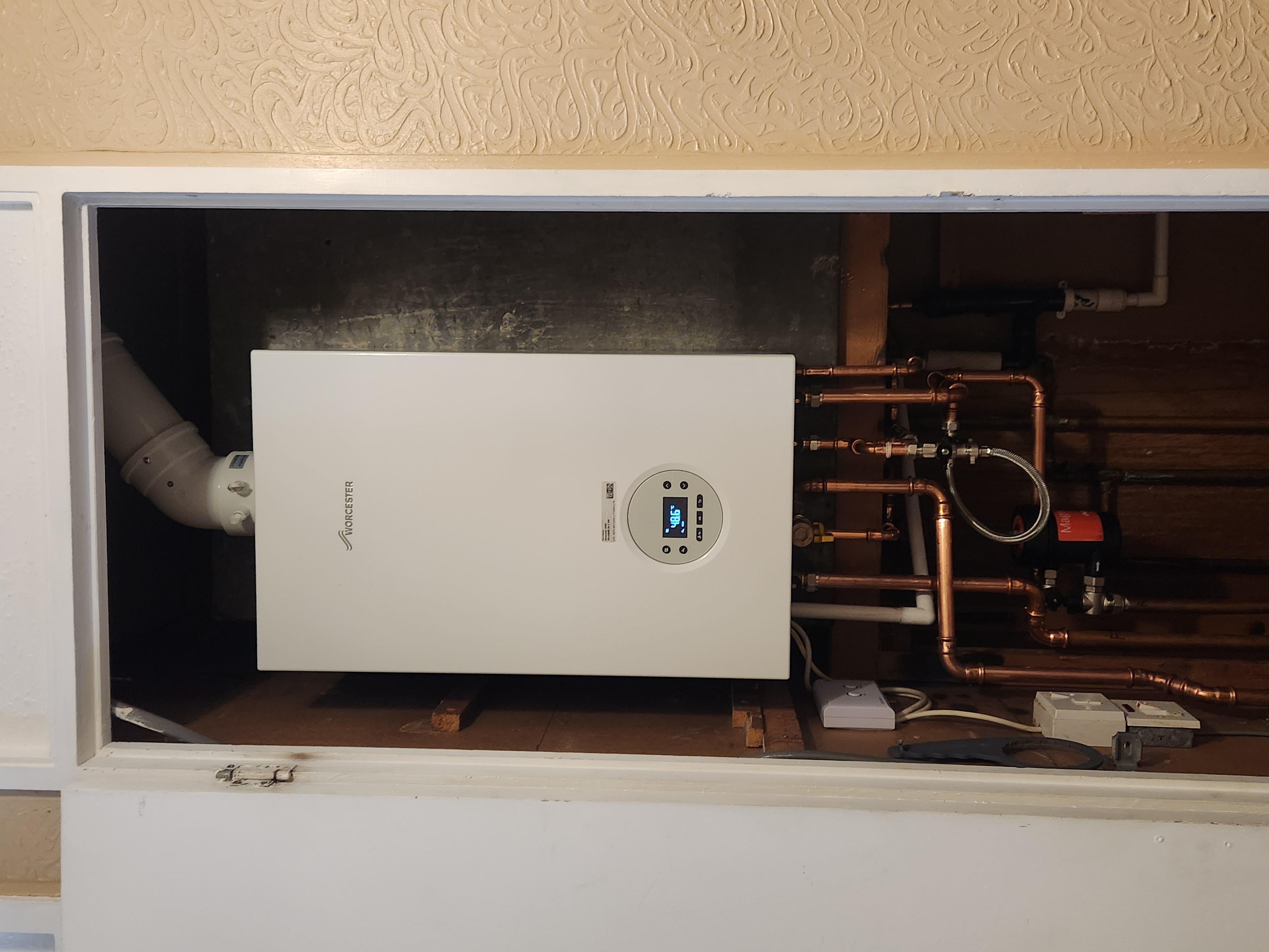 Worcester Bosch combi boiler installed within a cupboard with digital display, copper pipework and system components.