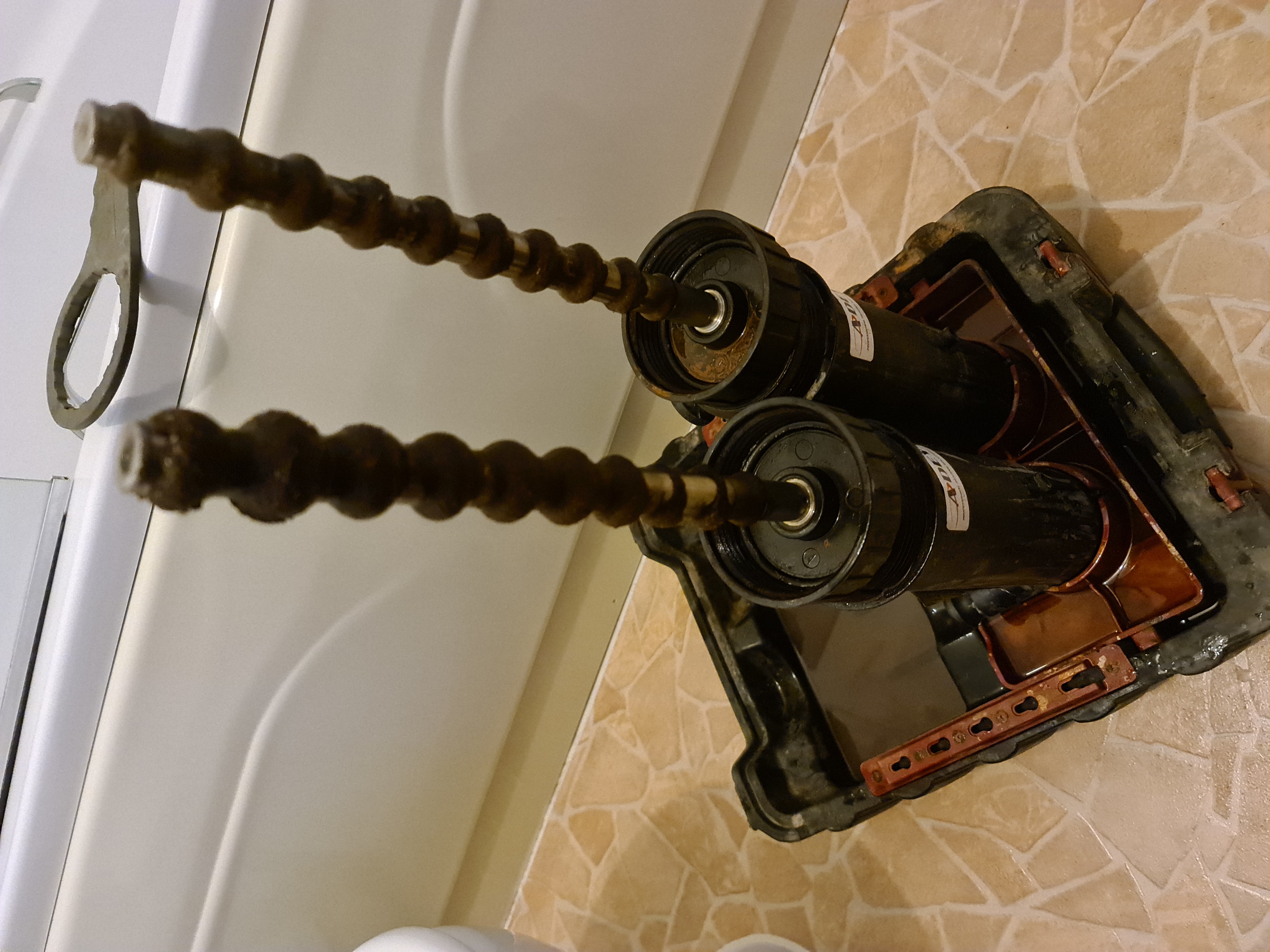 Rusty coiled drain cleaning rod alongside old mechanical pump equipment showing signs of corrosion and wear.