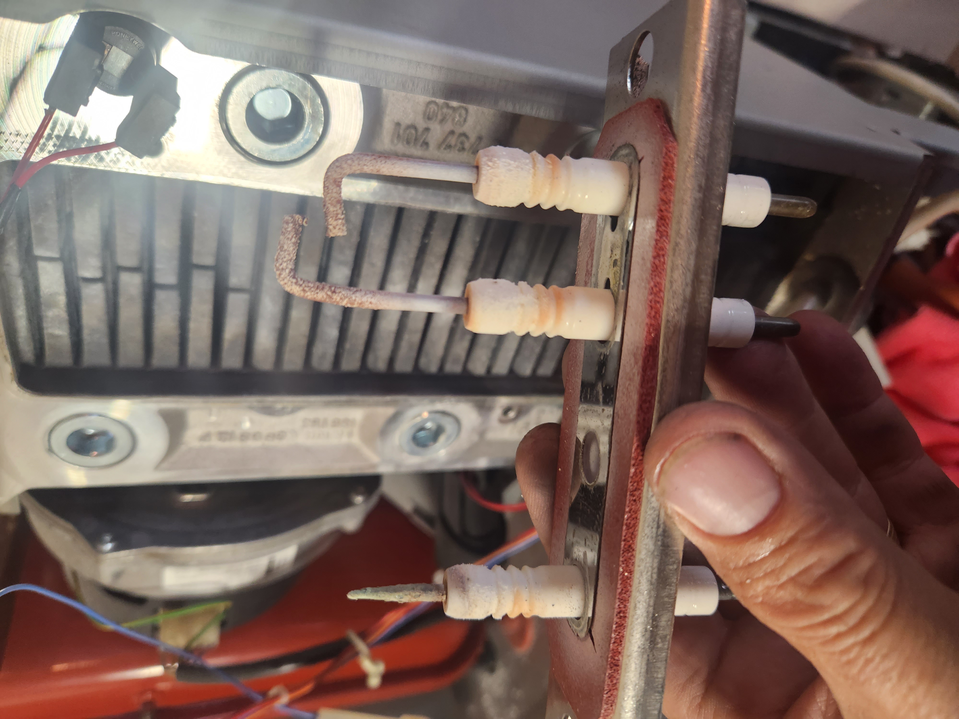 Close-up of gas burner ignition electrodes with worn ceramic tips being inspected during a service.