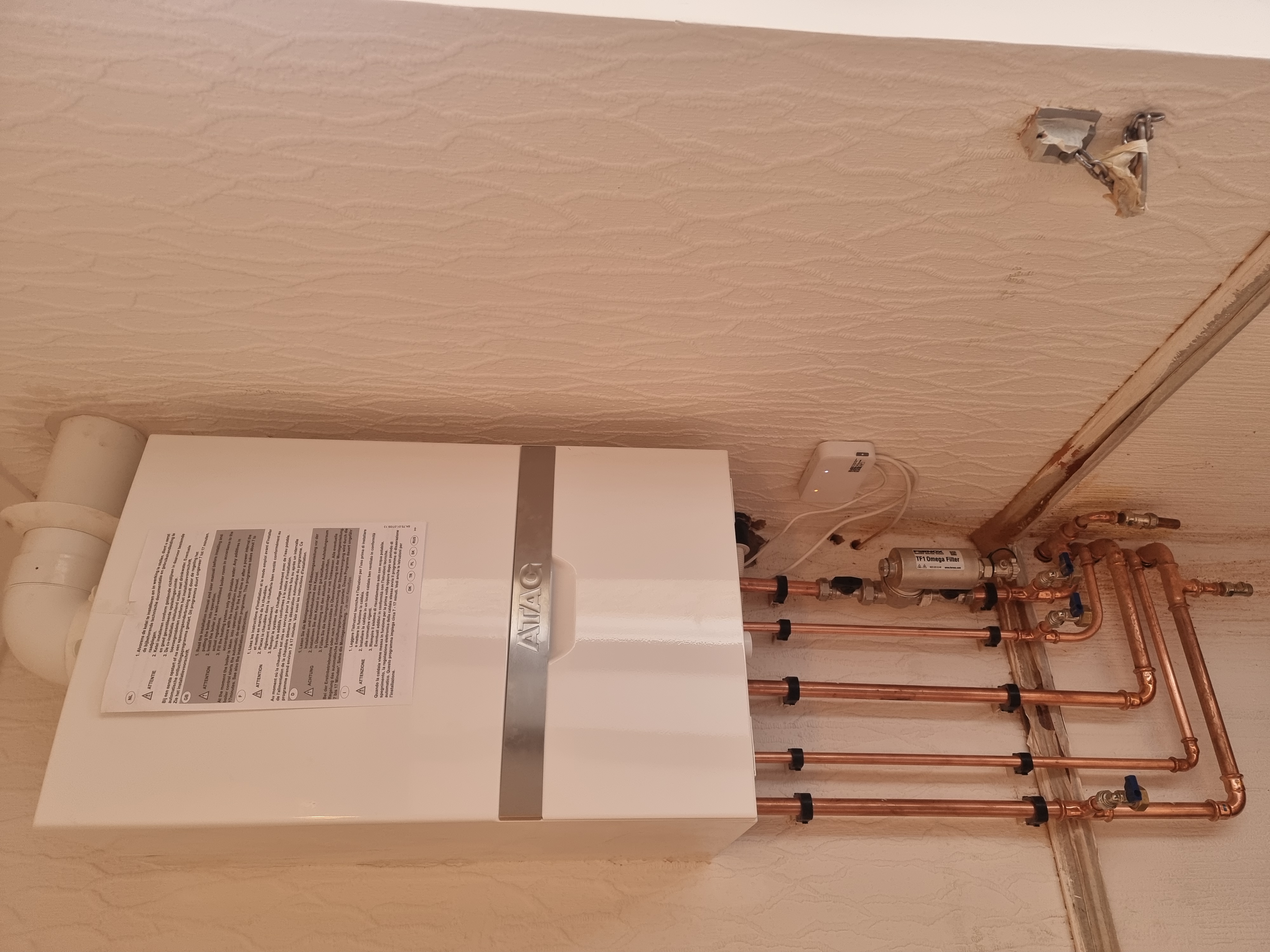 White ATAG boiler installed with Fernox TF1 Omega magnetic filter, copper pipework and smart thermostat in a cupboard space.