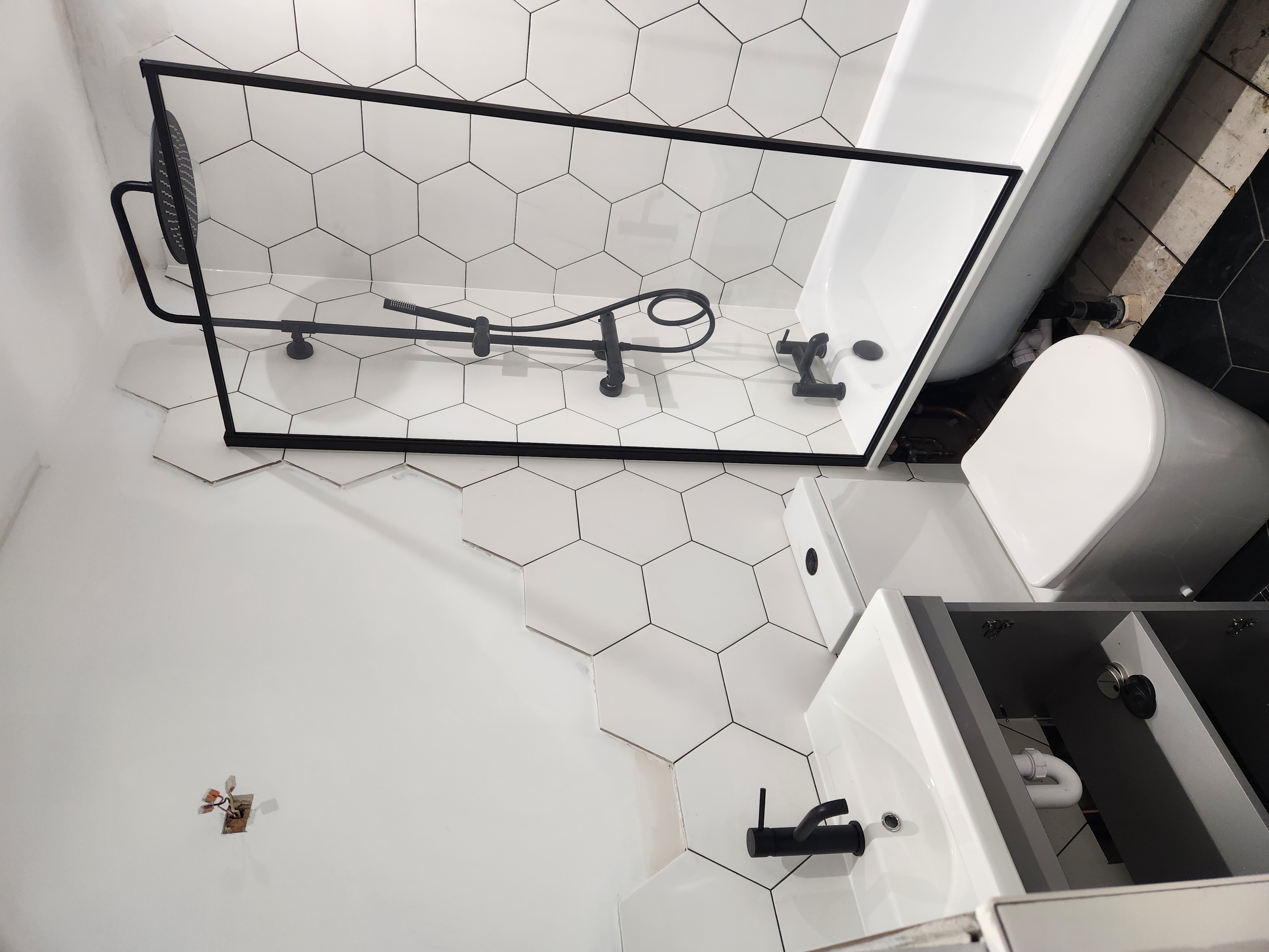 Modern bathroom with white hexagonal floor tiles, black-framed shower screen, freestanding bathtub and matte-black mixer taps.