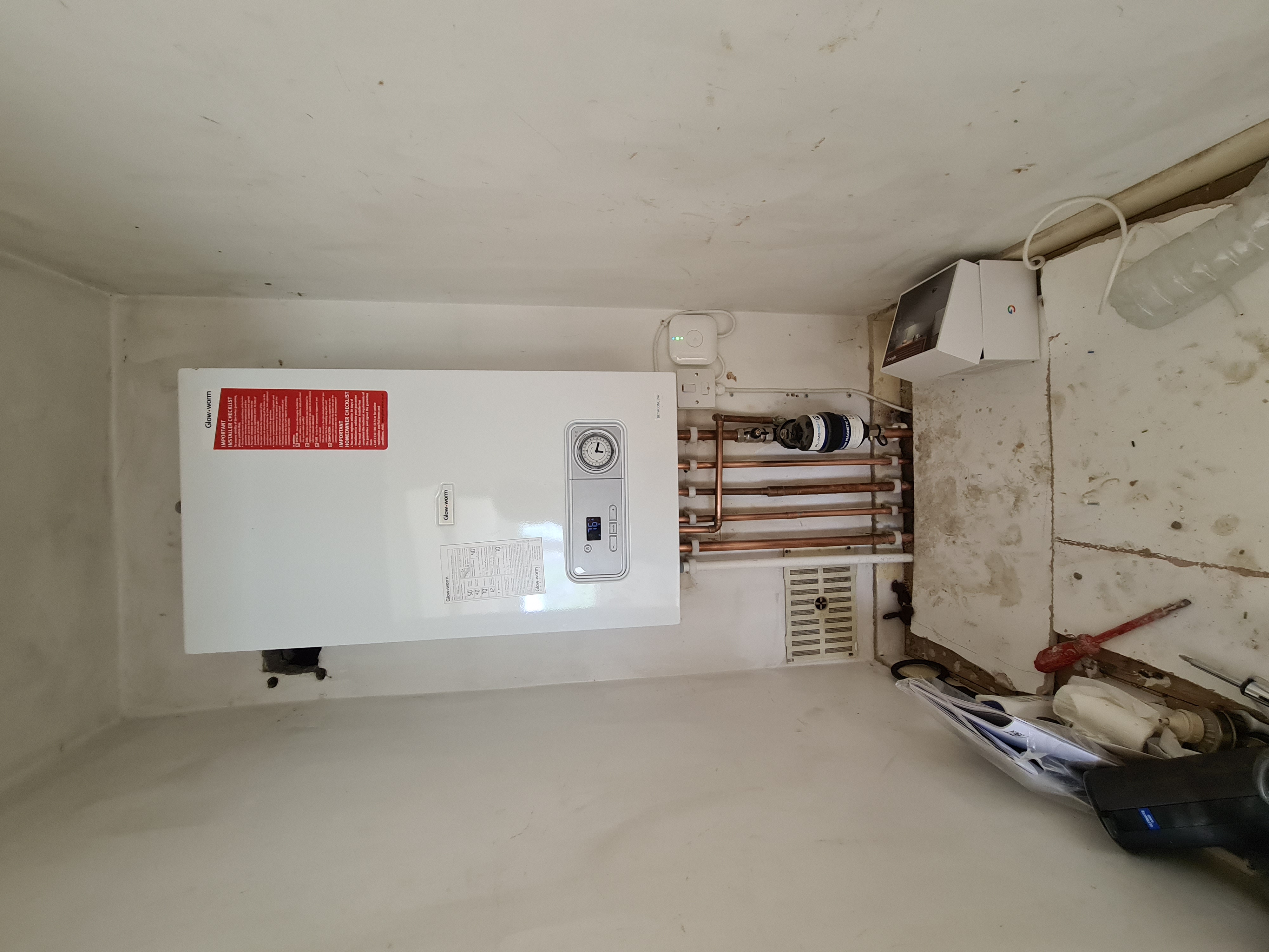 Glow-worm combi boiler mounted on a wall with copper pipework, magnetic filter and smart thermostat above.