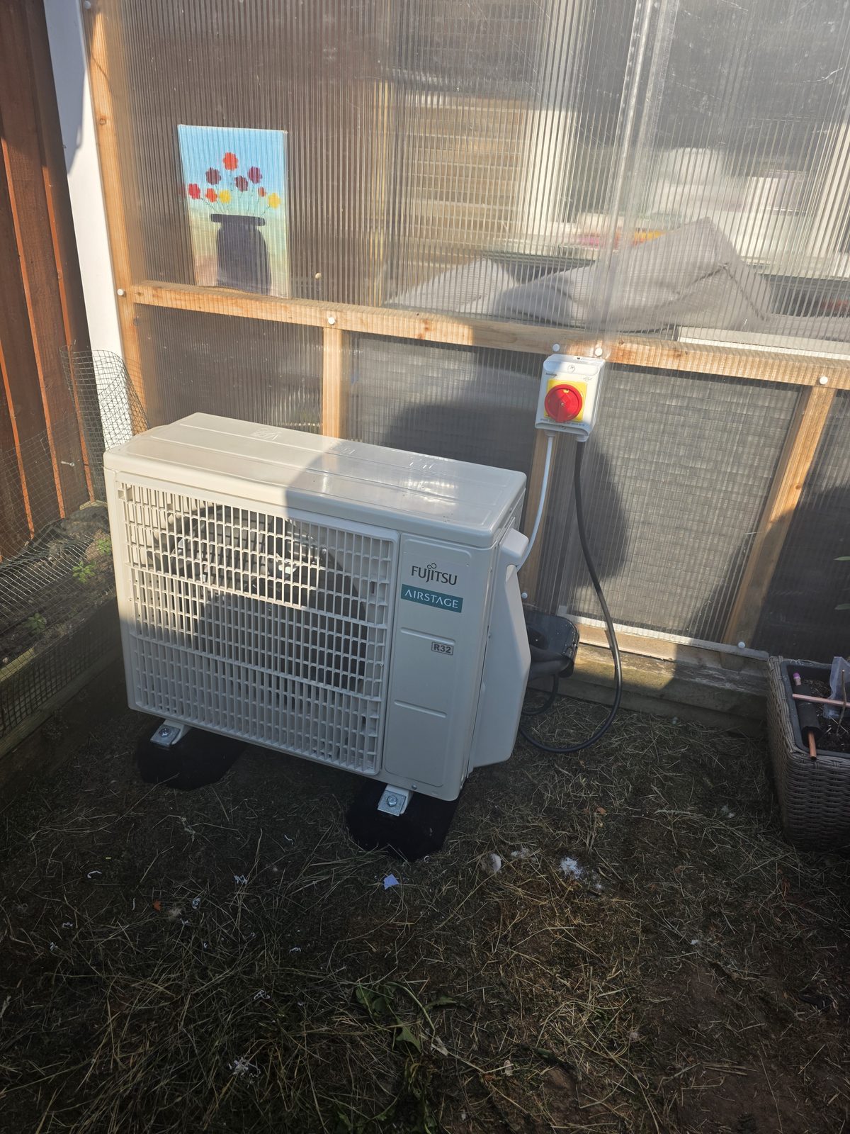 Outdoor Fujitsu air conditioning unit installed on the ground next to a structure.
