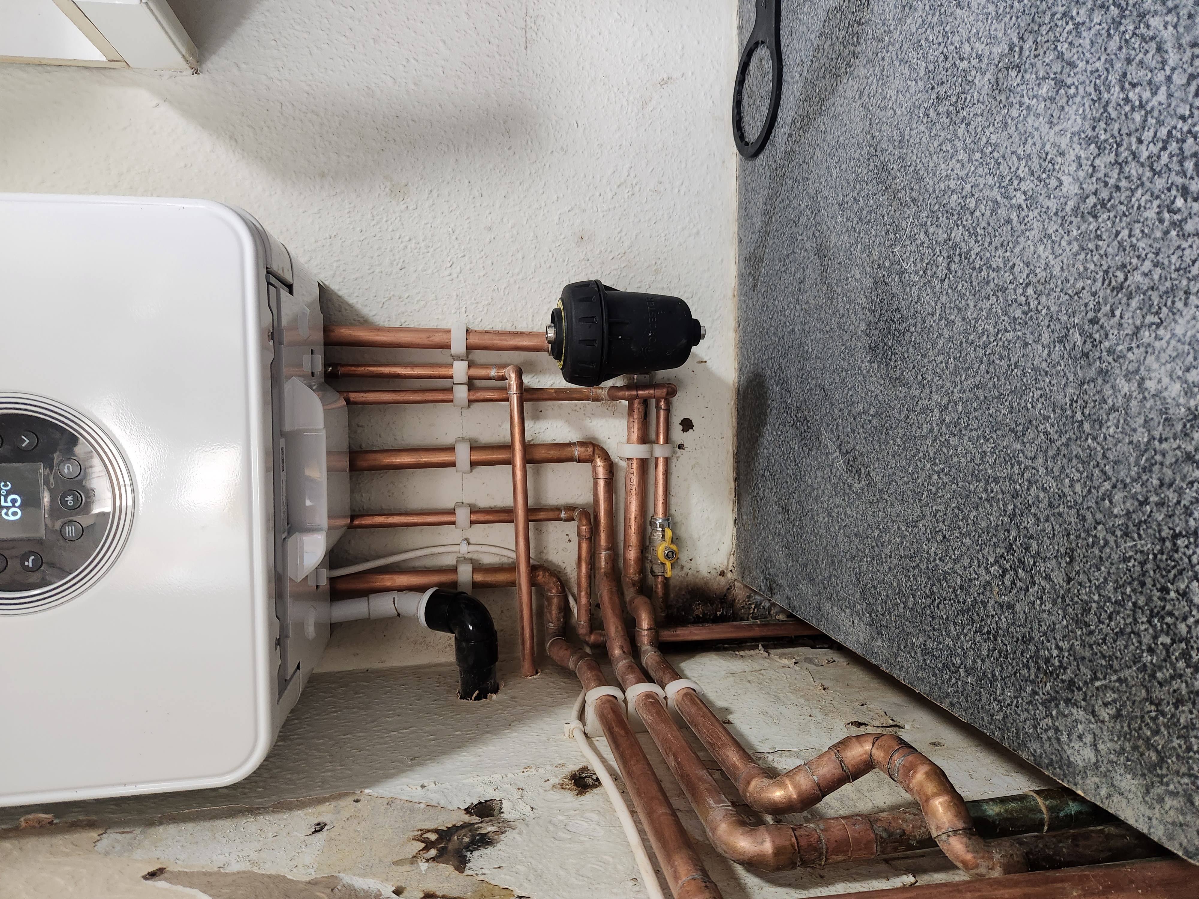 White combi boiler with digital display and neatly arranged copper pipework manifold with magnetic filter.