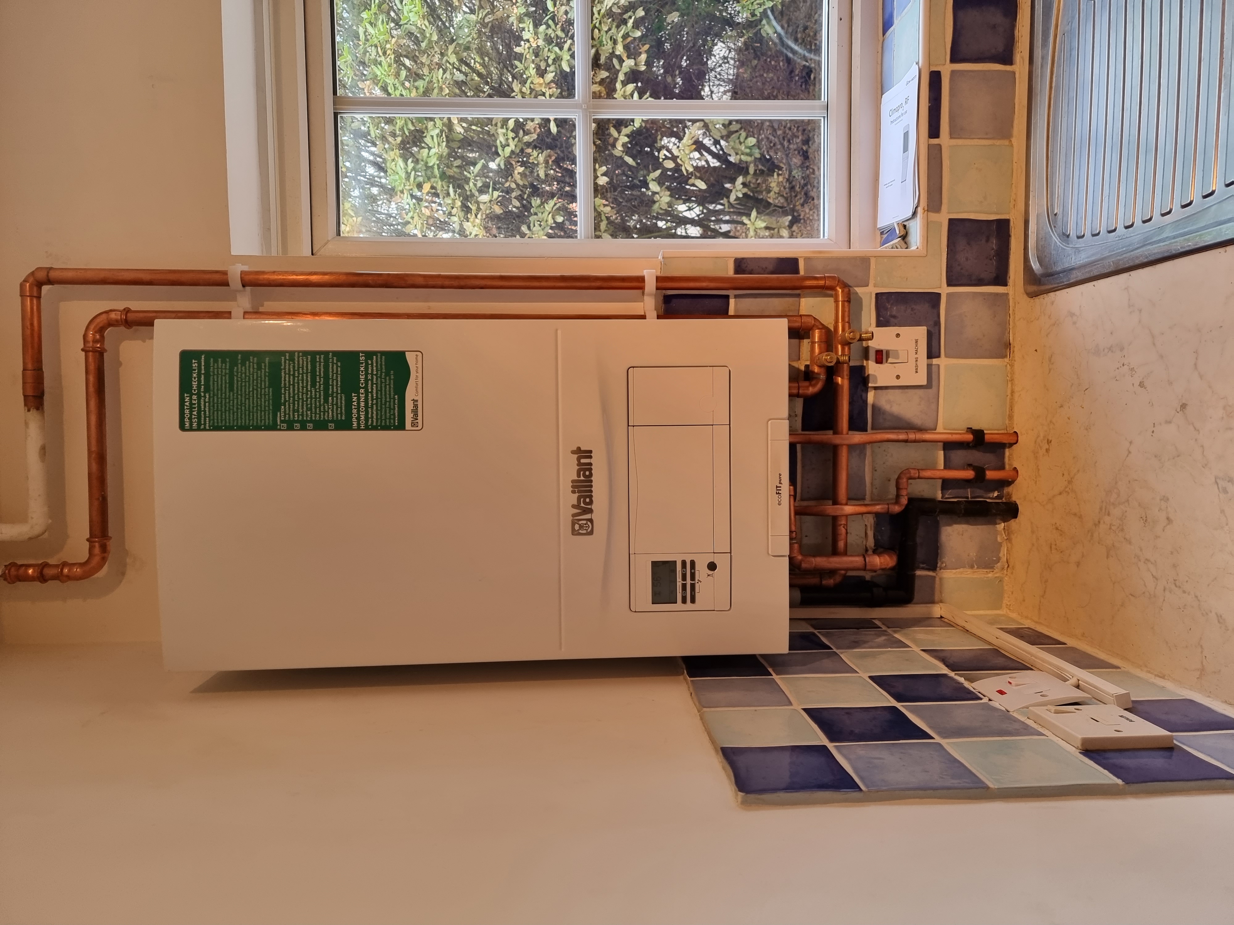 Vaillant ecoFIT pure boiler installed beneath a kitchen window with colourful tiled splashback and copper pipework.
