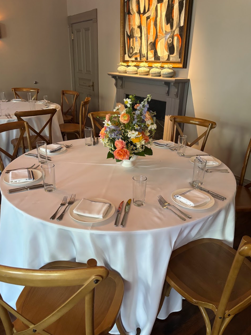Elegant round table set with white linens, crossback chairs, and vibrant peach coral blue floral centerpiece