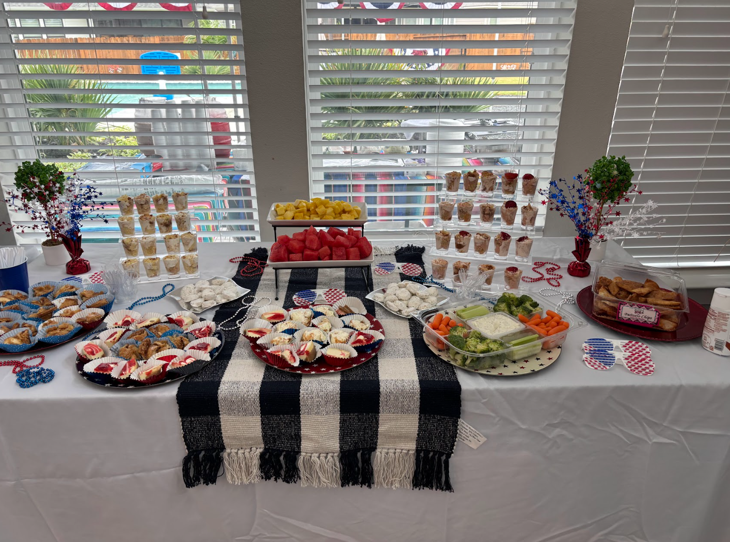 Party food table fully stocked with desserts, fresh watermelon, vegetables, dips, and festive red white and blue decorations