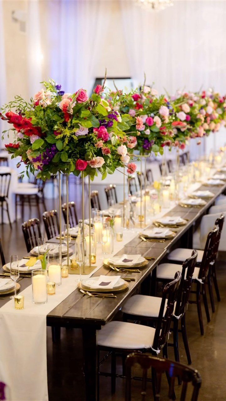 Long reception tables with tall colorful floral centerpieces, candles, and elegant place settings