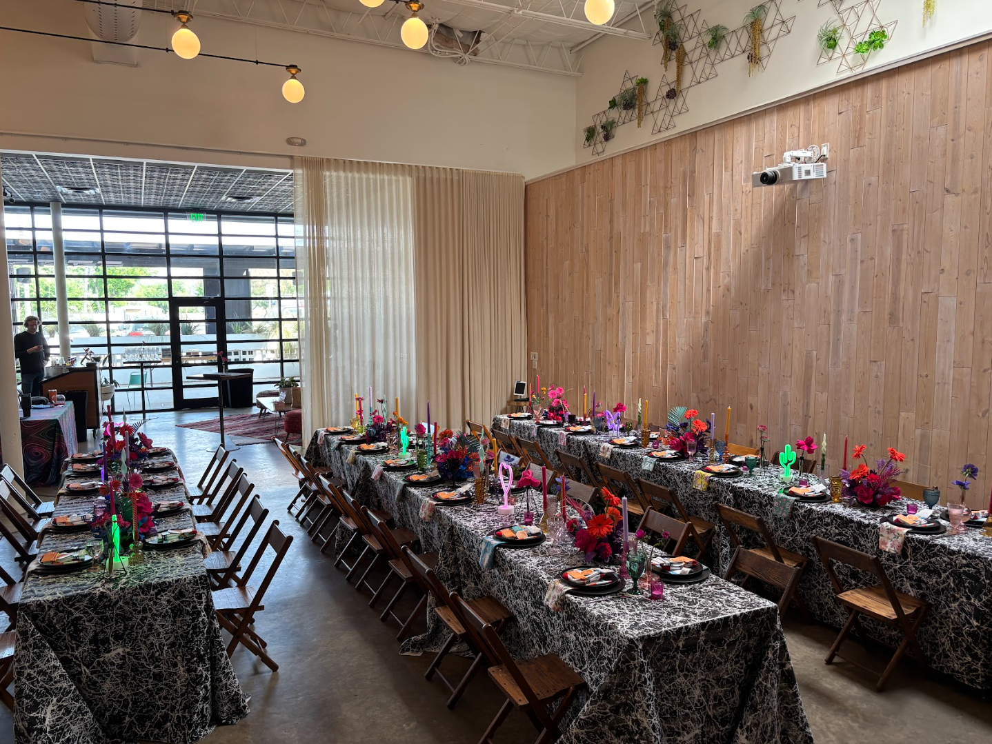 Modern venue with long reception tables set with bold colorful floral centerpieces and complete place settings awaiting guests