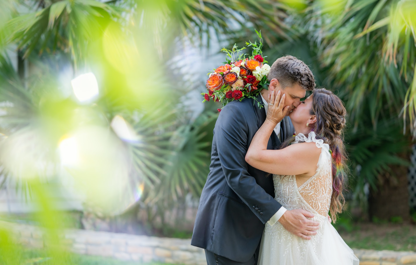 Bride and groom sharing a kiss at their wedding, bride holding a vibrant orange and red bouquet
