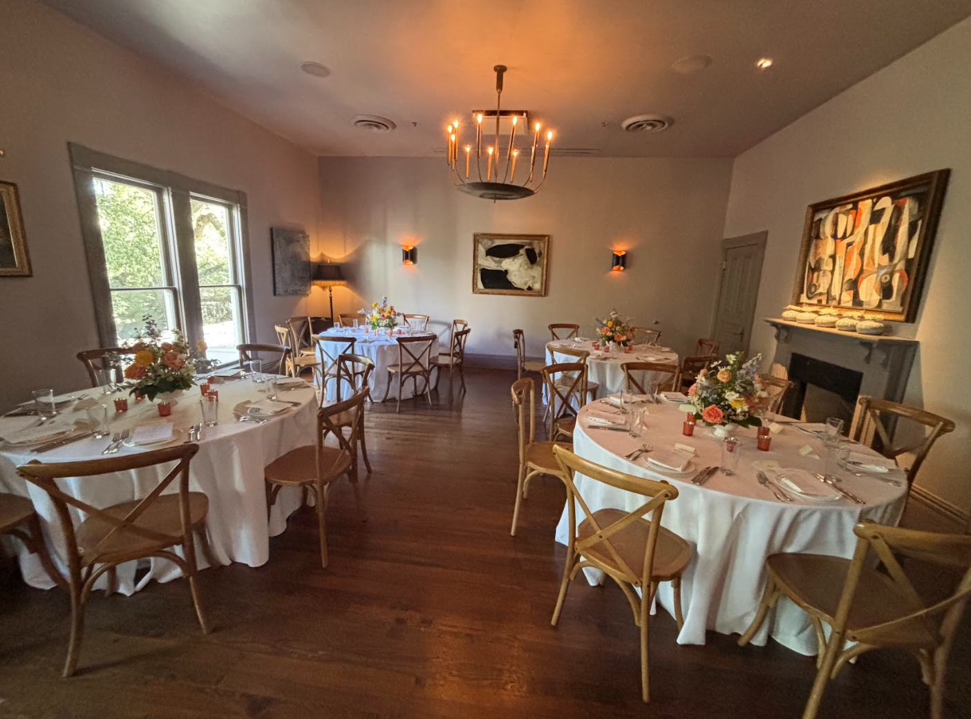 Elegant event room with round tables, white linens, wooden crossback chairs, and fresh floral centerpieces