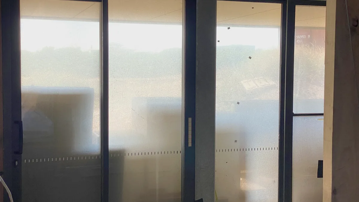 Sliding doors covered in construction dust with manufacturer labels and safety decals still attached