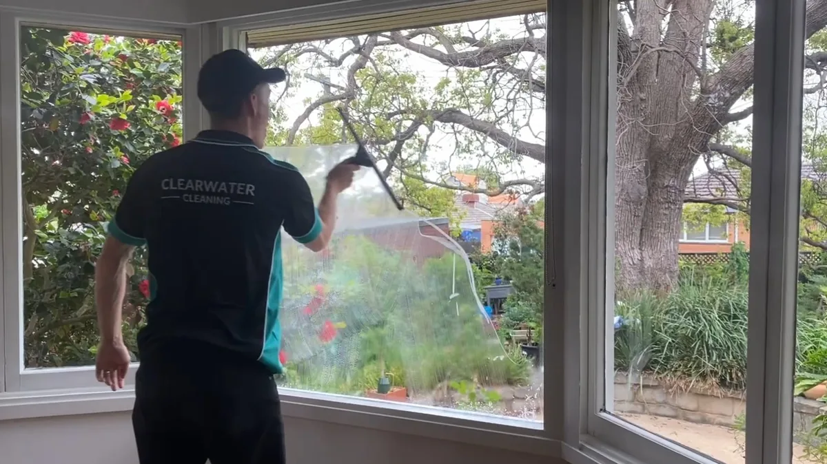 Clearwater Cleaning technician in uniform cleaning the inside of a bay window