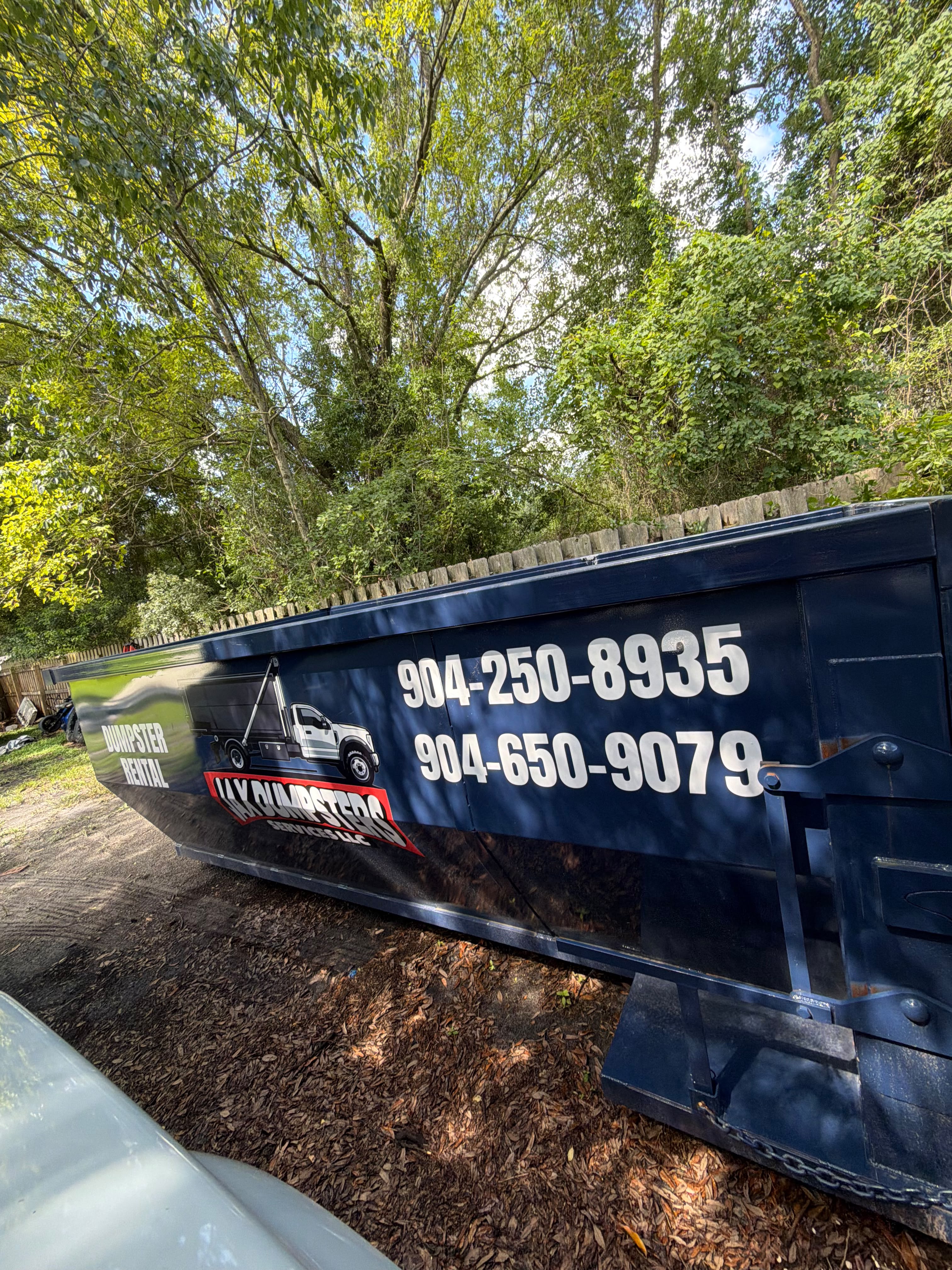 Dark blue JAX Dumpsters rental container with company branding and phone numbers on residential driveway