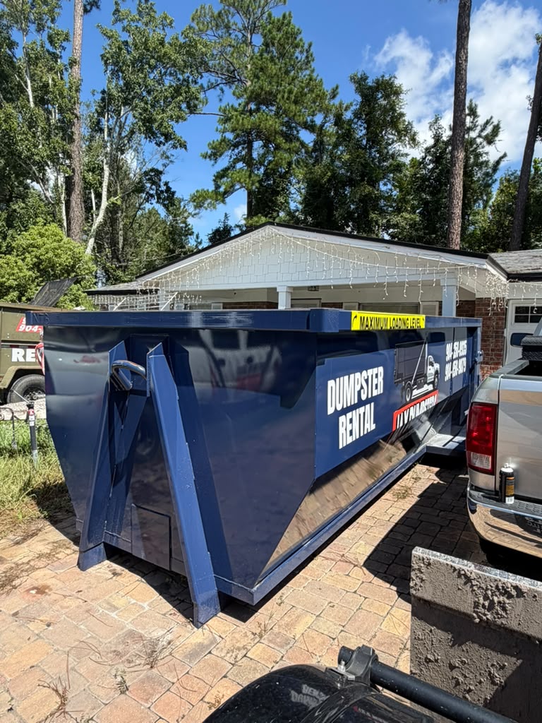 Large blue JAX Dumpsters rental container with DUMPSTER RENTAL signage on driveway