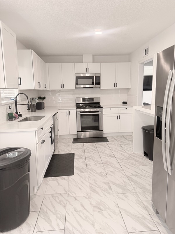RCS Legacy Living kitchen with white cabinetry, stainless steel appliances, marble tile flooring, and coffee station