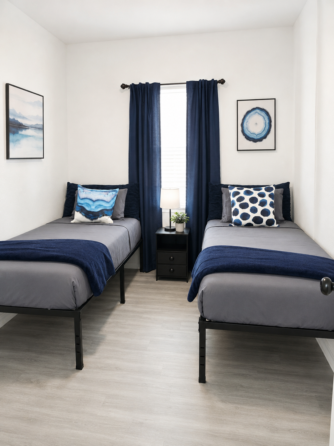 RCS Legacy Living furnished bedroom with twin beds, navy bedding, artwork, and residential ambiance