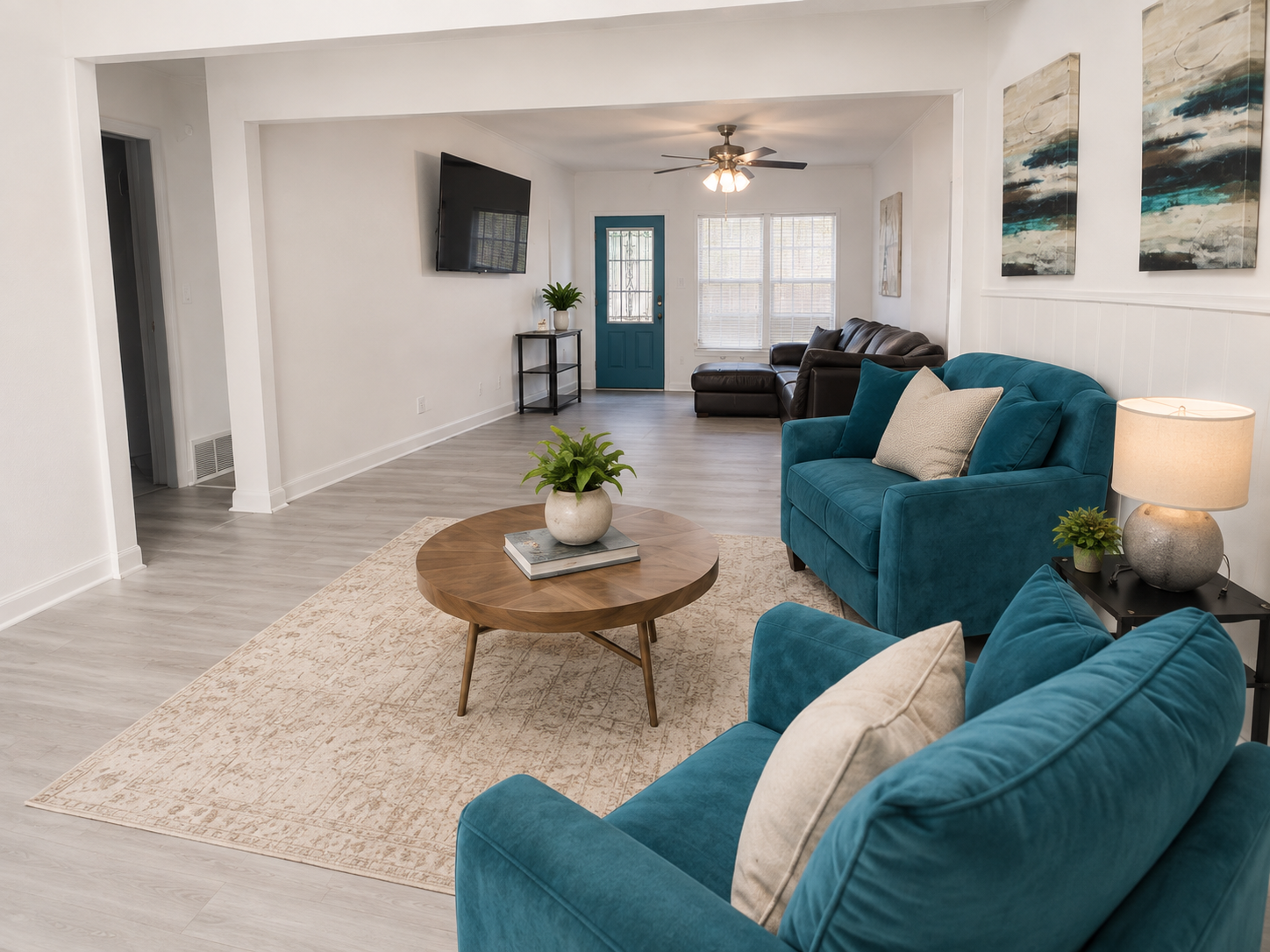 RCS Legacy Living living room with teal velvet seating, leather sofa, light wood flooring, teal front door, and welcoming open floor plan
