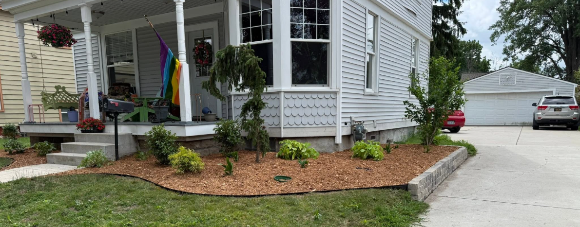 Newly mulched garden bed with small plants along a stone foundation wall in West Michigan