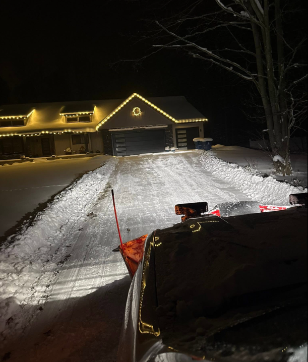 Snow plow truck plowing driveway surrounded by trees