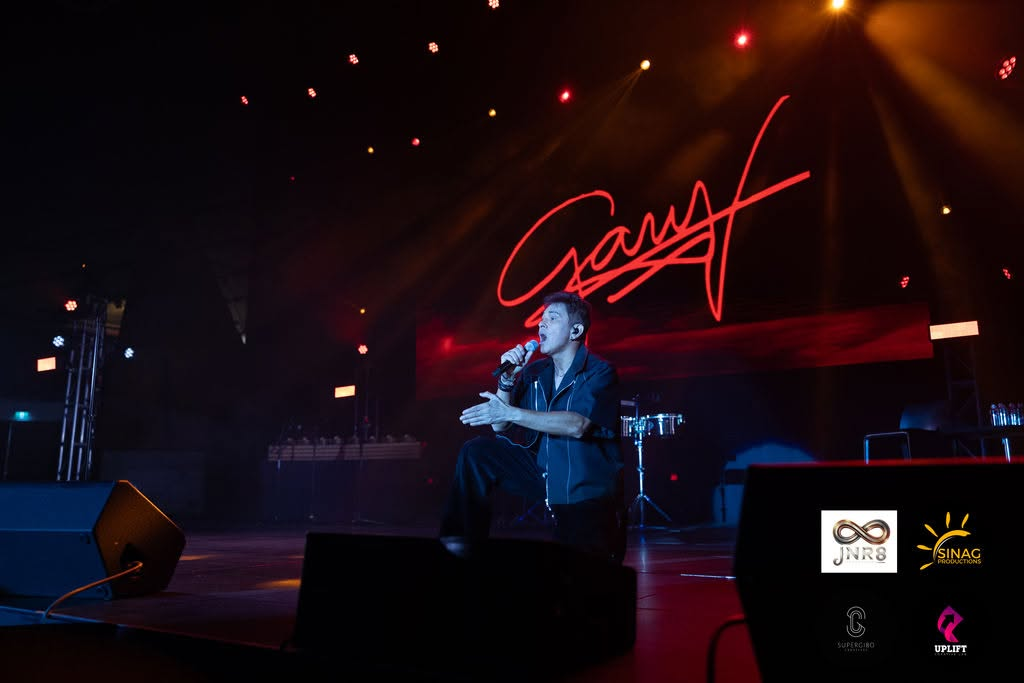 Gary V singing passionately on bended knee against a glowing red backdrop illuminated by his iconic signature logo.