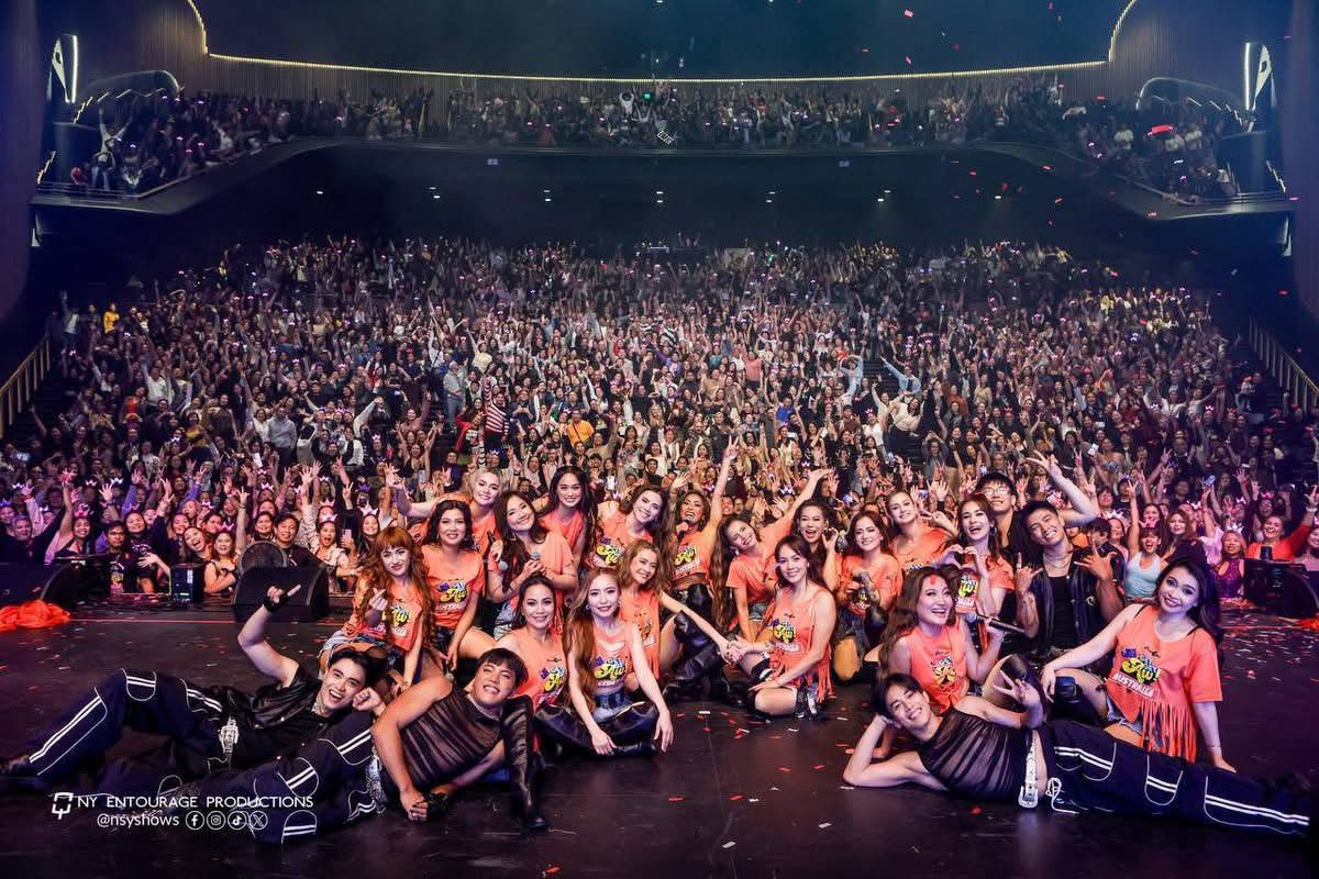 The SexBomb Girls and cast posing on stage with an electric, packed arena crowd in matching Get, Get Aw! Australia reunion tour gear.