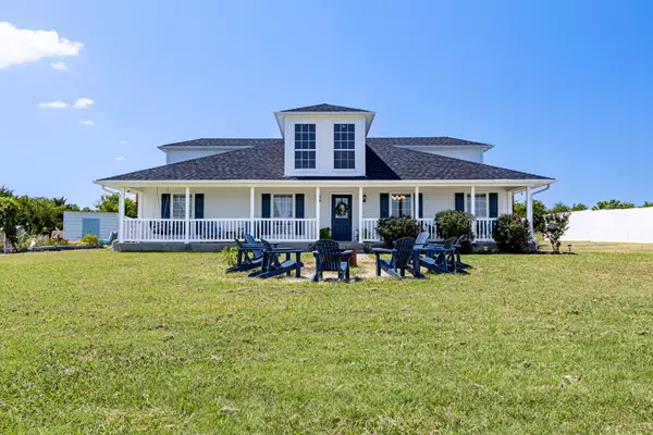 Beautiful white farmhouse with wrap-around porch and outdoor seating on a green lawn