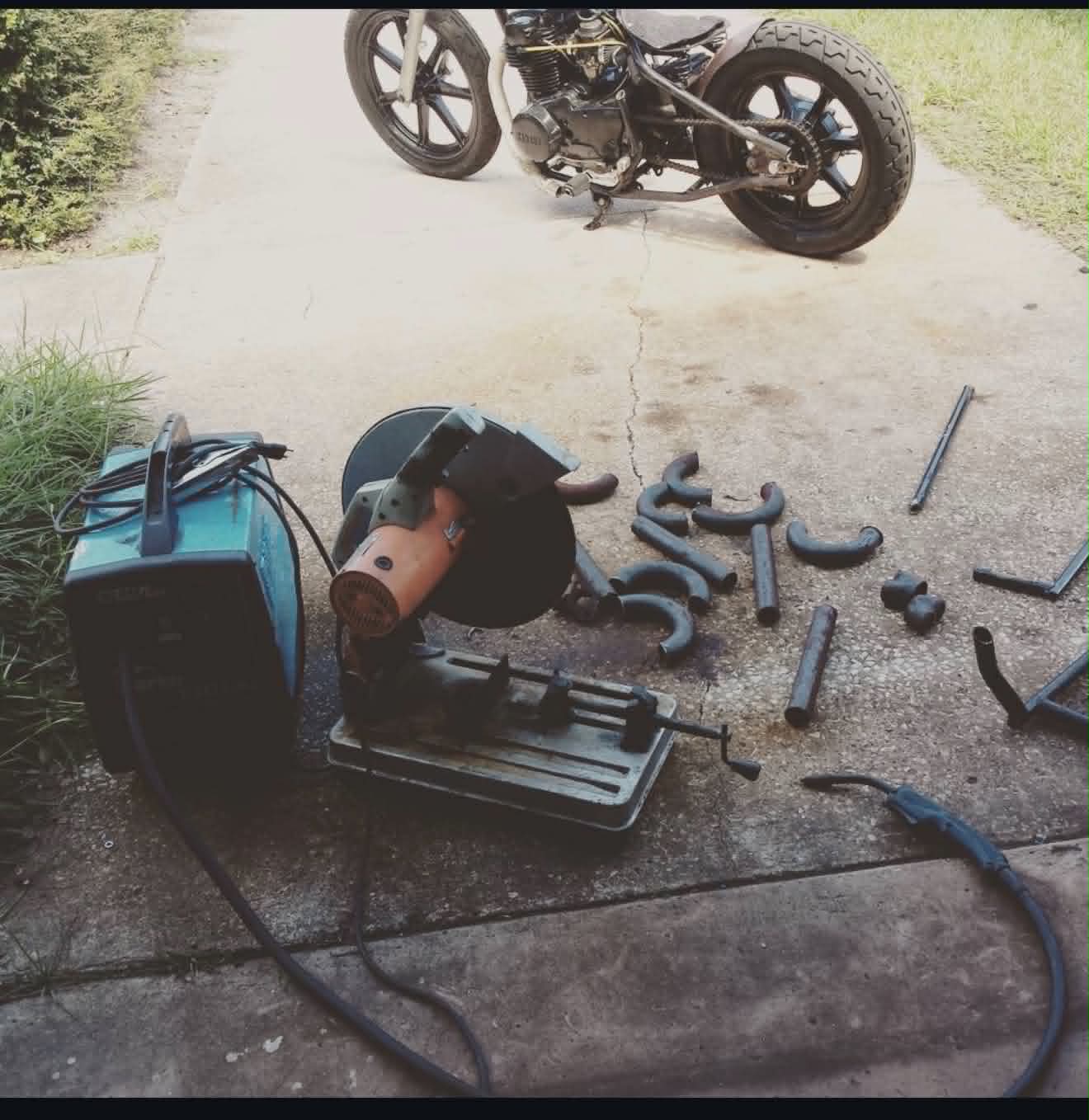 Motorcycle fabrication workshop showing custom pipe bending and welding setup