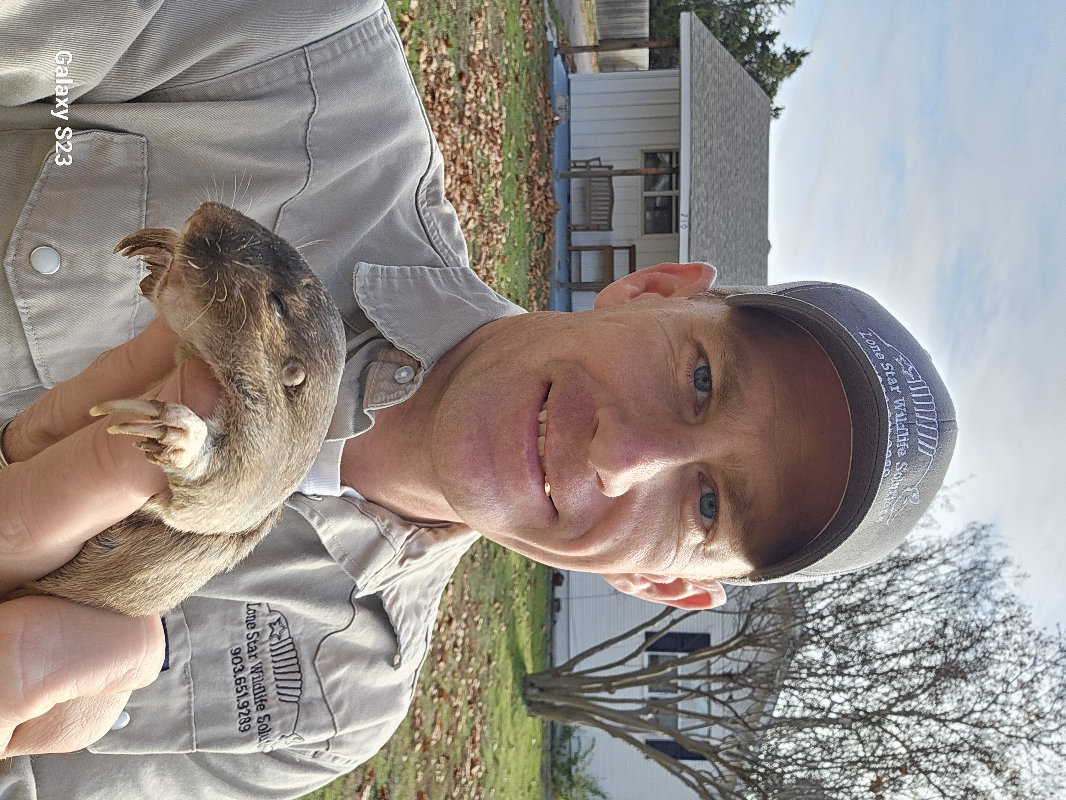 Lone Star Wildlife Solutions technician in branded shirt and cap holding live captured gopher showing brown fur prominent front digging claws and small rounded ears