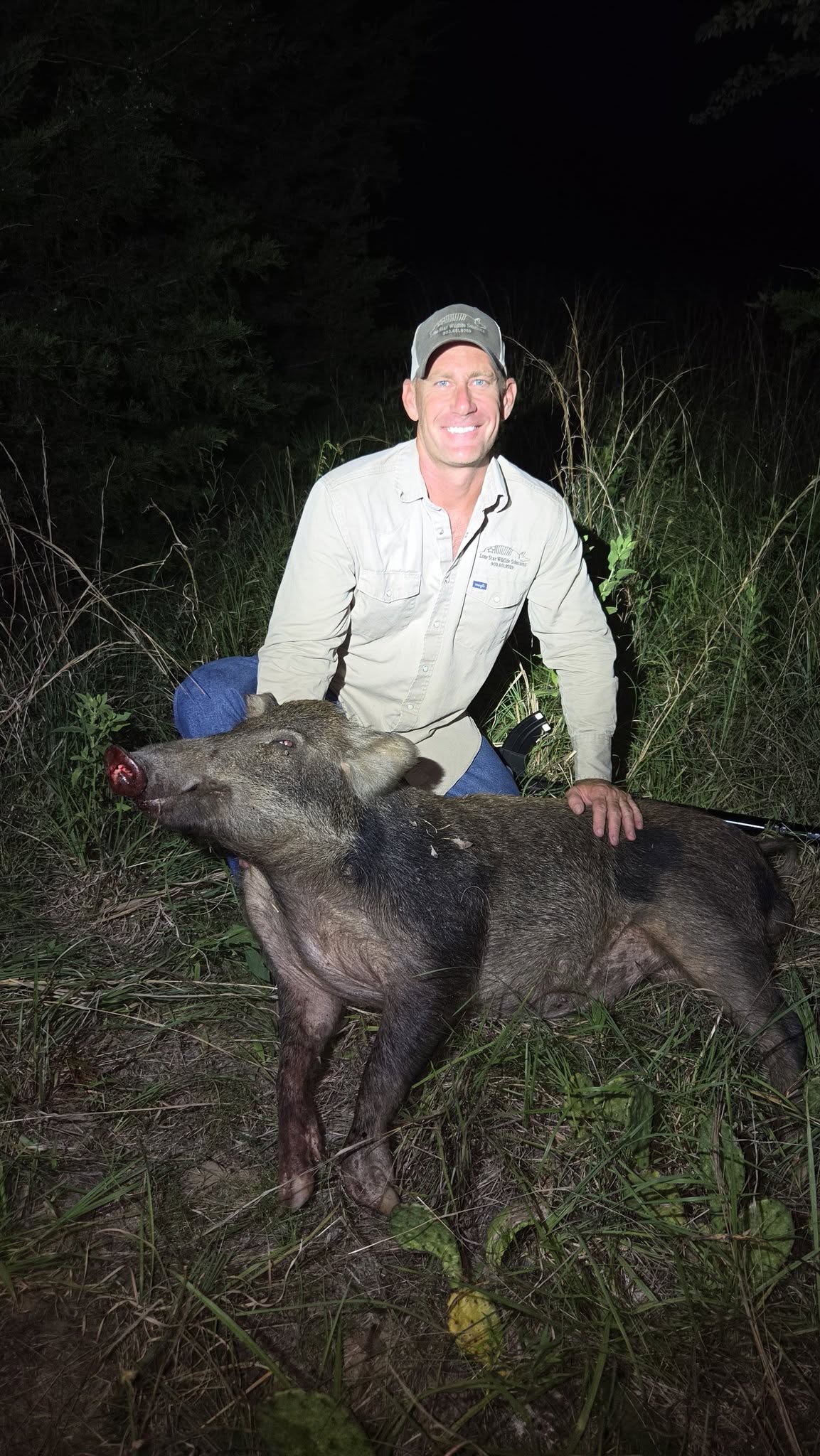 Lone Star Wildlife Solutions technician kneeling at night with large captured trophy feral boar showing tusks