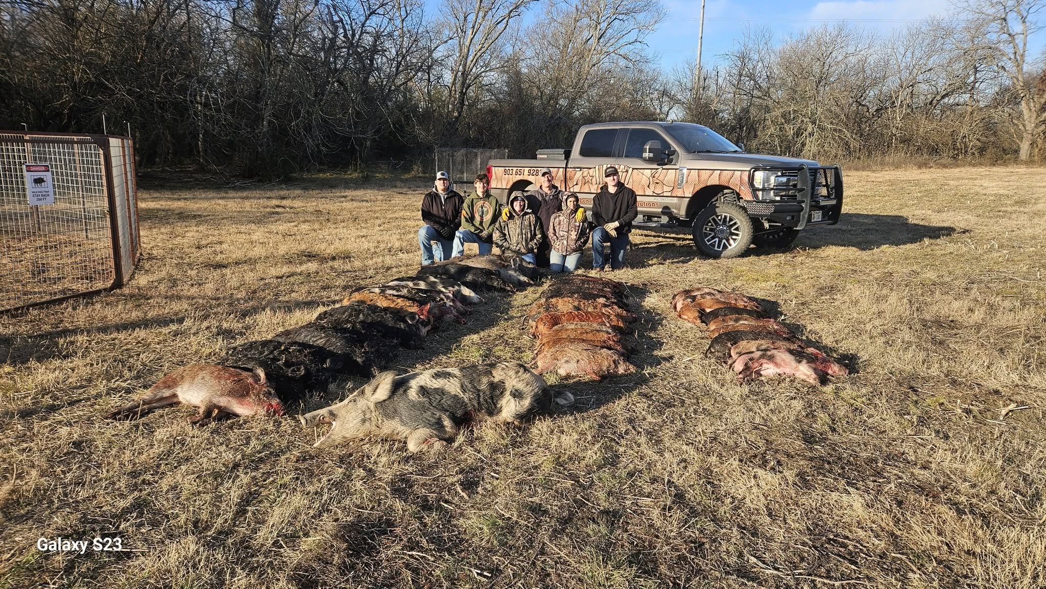 Full Lone Star Wildlife Solutions team of five posing with branded pickup truck behind entire captured feral hog sounder laid out in rows on dry pasture