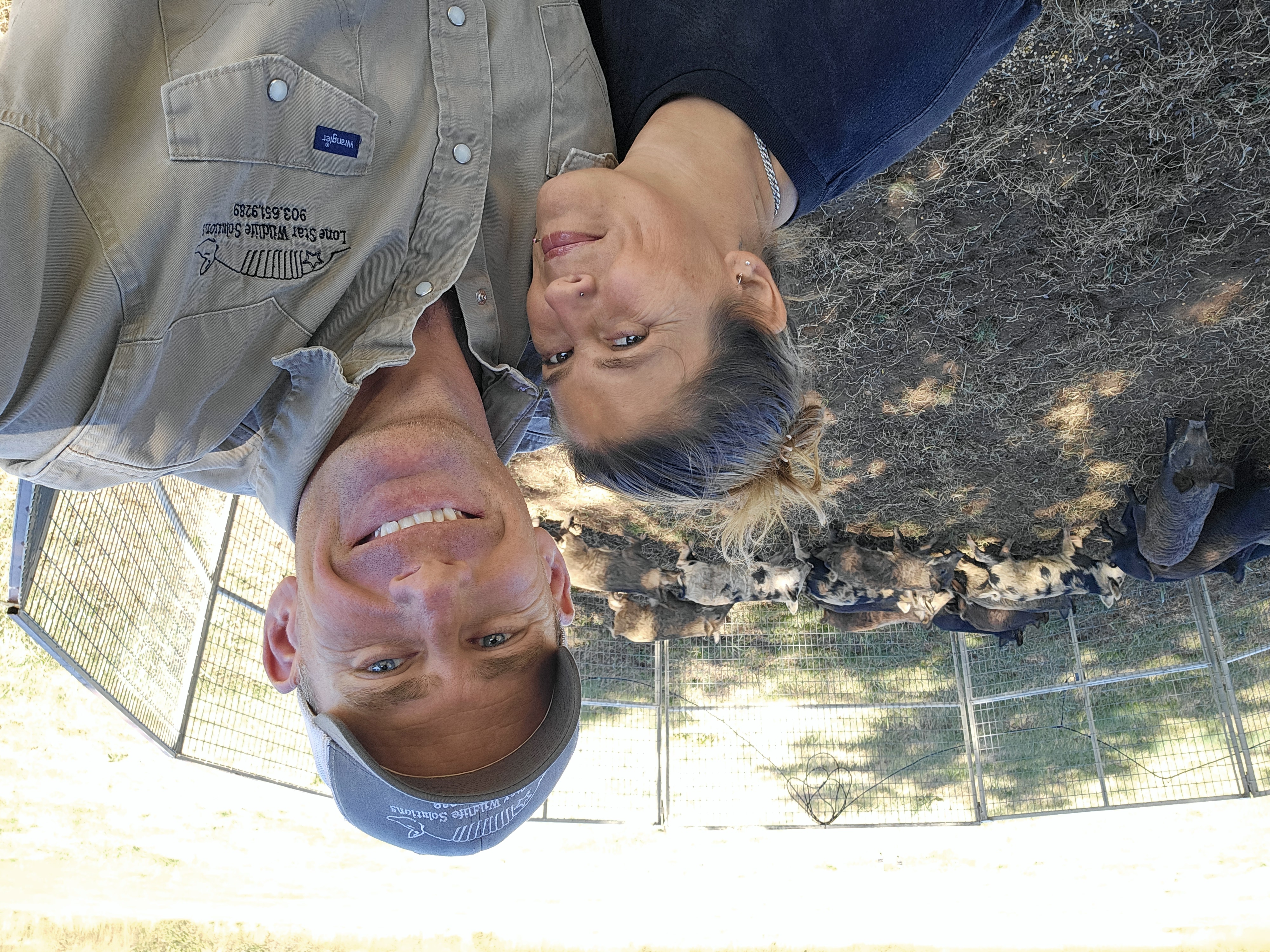 Lone Star Wildlife Solutions team taking selfie photo with captured feral hog sounder lined up on ground behind wire fence