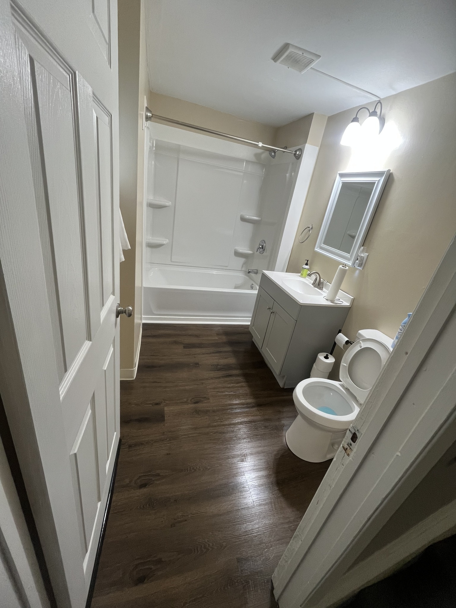 Spotlessly clean modern bathroom with vanity, mirror, tub, and wood-look floors
