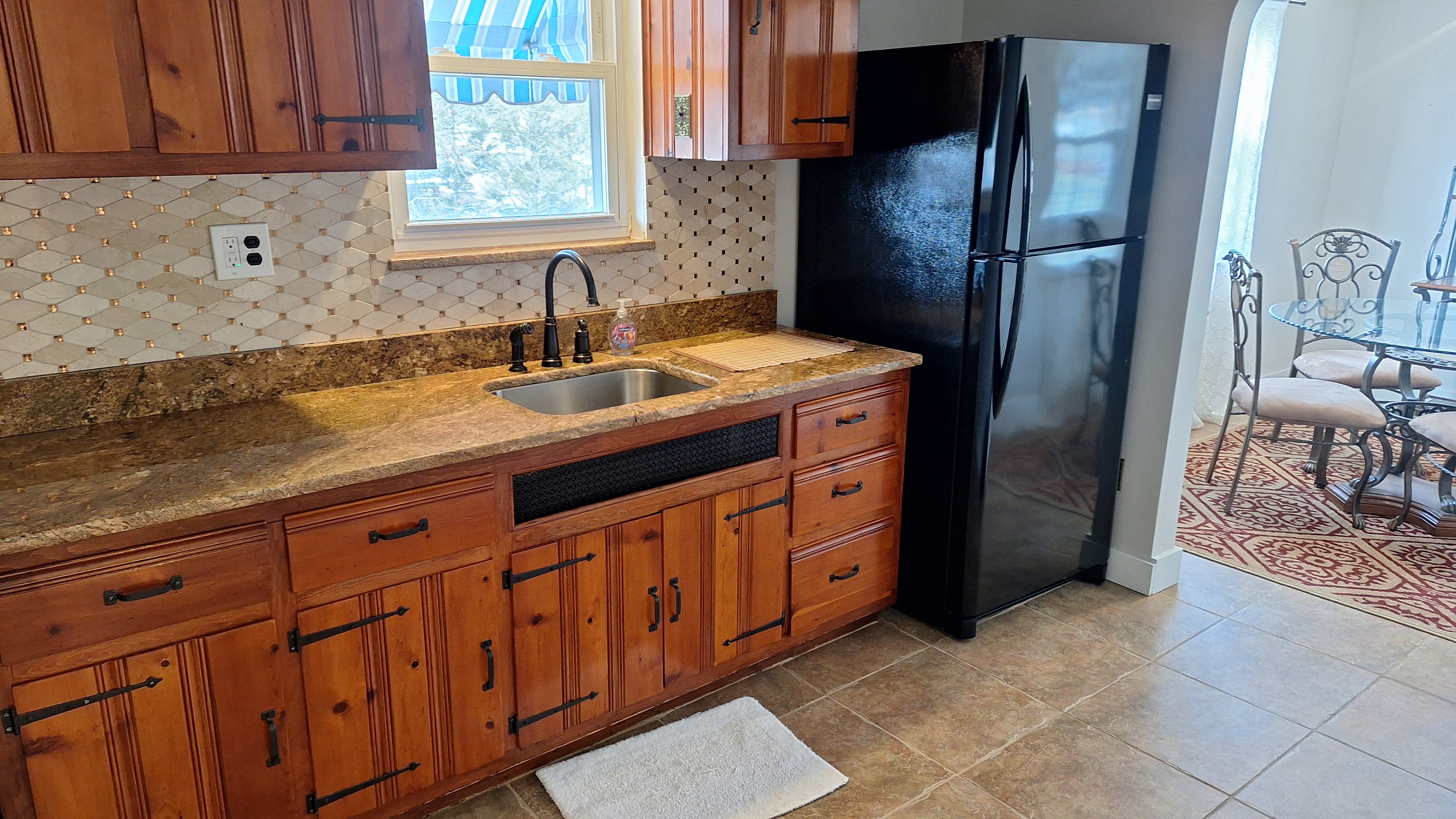 Spotless kitchen with wood cabinetry, stainless sink, and clean black refrigerator